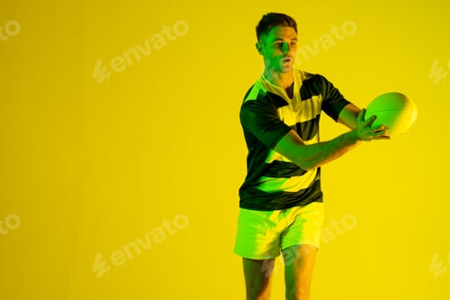 Preview: Caucasian male rugby player catching rugby ball over yellow lighting