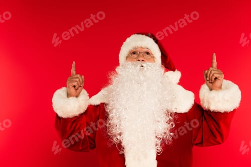 Preview: Santa claus in eyeglasses pointing with fingers on red background