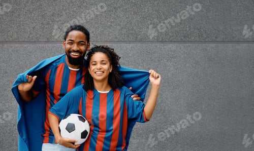 Preview: Happy black couple of soccer fans cheering during the world cup and looking at camera.