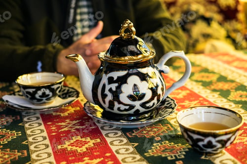 Preview: Traditional Uzbekistan tea set on a colorful patterned tablecloth, with a person's hands