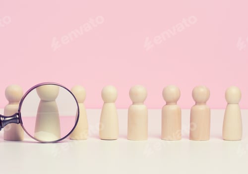 Preview: Wooden figures of men stand on a pink background and a red plastic magnifying glass.