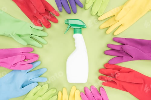 Preview: top view of multicolored rubber gloves in circle around spray bottle with detergent on green