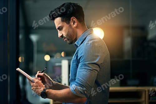 Preview: Shot of a young businessman making notes in a notepad during a late night at work