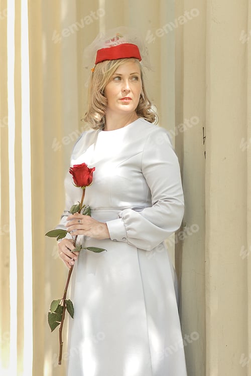 Preview: Young woman in vintage red hat and retro blue dress walking in summer park.