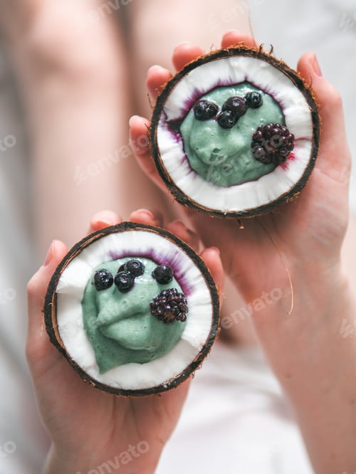 Preview: Two coconut half spirulina smoothie in woman hands