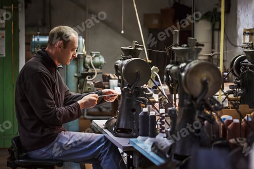 Preview: Man sitting at a sewing machine in a shoemaker's workshop.