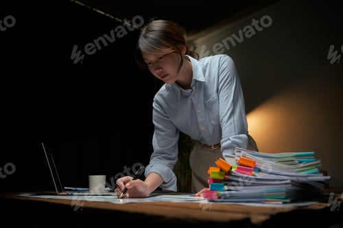 Preview: Young businesswoman working late reviewing financial documents