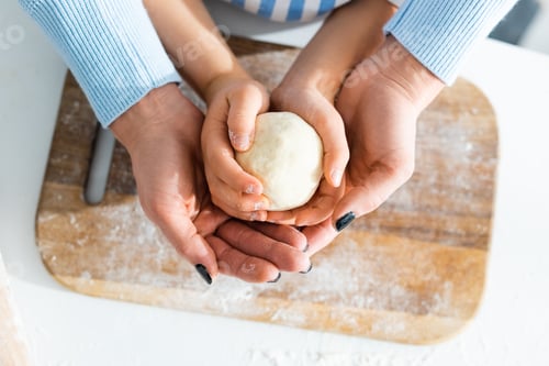 Preview: cropped view of mother and daughter holding dough in kitchen