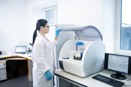 Preview: Dark-haired doctor in a white robe opening the hematological analyzer