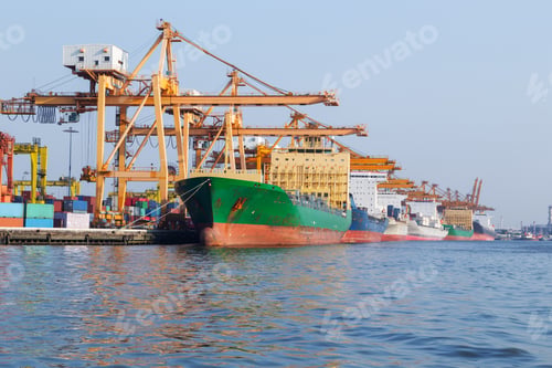 Preview: Cargo ships dock at a busy port terminal alongside towering yellow gantry cranes