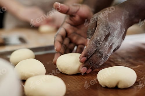 Preview: Close up of male hands carefully shaping dough buns working in bakery kitchen