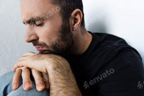 Preview: adult depressed man suffering while sitting by white wall with closed eyes