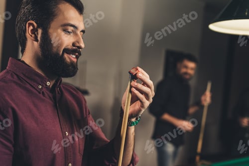Preview: handsome man rubbing cue with chalk at bar with friends
