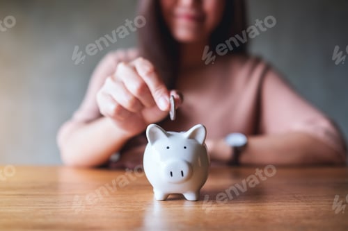 Preview: Closeup image of a woman putting coins into piggy bank for saving money concept