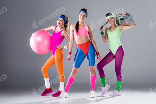 Preview: beautiful sporty girls with sports equipment and tape recorder smiling at camera on grey