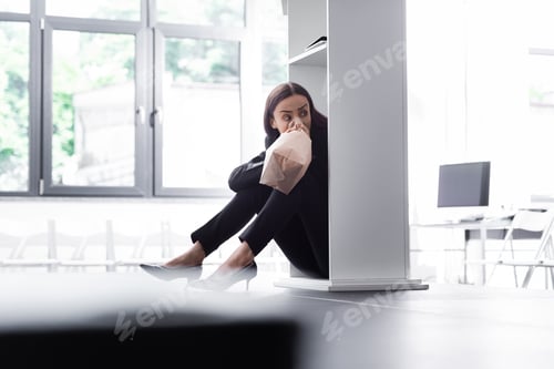 Preview: selective focus of young lecturer sitting on floor and hiding behind podium tribune, while suffering
