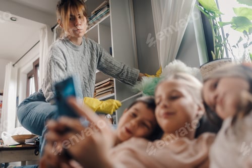 Preview: Mother cleaning while children using smartphones at home