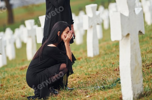 Preview: Two young women in black clothes visiting cemetery with many white crosses