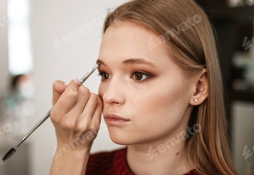 Preview: makeup artist applies eyebrow shadow on a beautiful young woman blonde model, face make up concept,