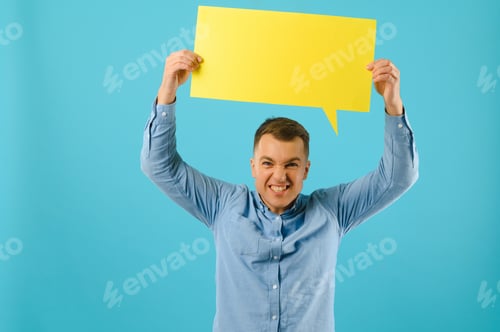 Preview: Handsome smiling man holding blank speech bubble sign isolated on light blue studio banner