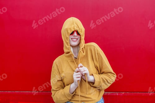 Preview: Albino woman in yellow hoodie smiling against a bright red background
