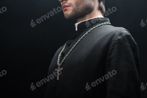 Preview: cropped view of catholic priest in black cassock with silver cross on necklace isolated on black