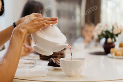 Preview: Woman hands pouring tea with a white pot at the table