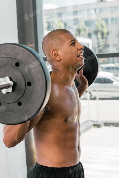 Preview: side view of muscular bare-chested african american sportsman lifting barbell in gym