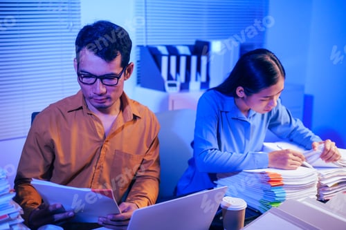 Preview: A businessman and woman are working overtime at their desks office at night.They are busy,stressed