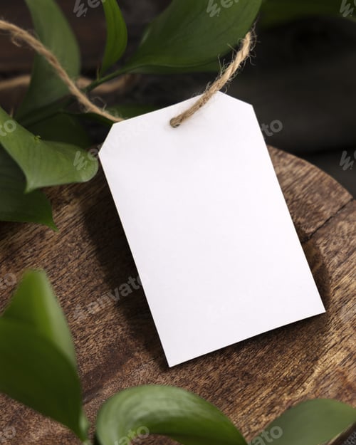 Preview: Vertical gift tag mockup on brown wooden tray near green leaves and grey fabric closeup