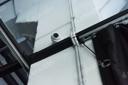 Preview: low angle view of monitoring camera on metal construction near white wall