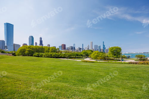 Preview: Sunny view of downtown Chicago with iconic skyscrapers rising above a lush green park meadow