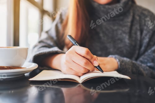 Preview: Closeup image of a woman writing on a blank notebook on the table
