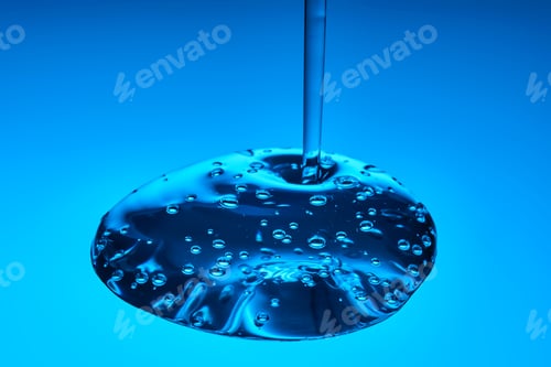 Preview: The viscous gel serum for the face flows and collects into a drop on a blue background..