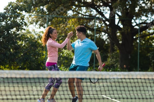 Preview: Smiling biracial couple playing tennis shaking hands on outdoor tennis court