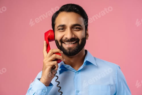 Preview: Portrait of smiling, handsome Indian man holding red phone, answering call, looking at camera