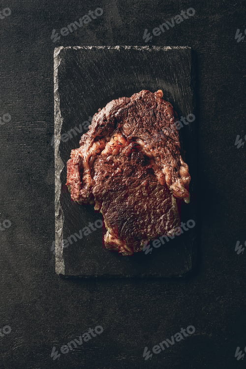 Preview: top view of roasted steak on black wooden board in kitchen