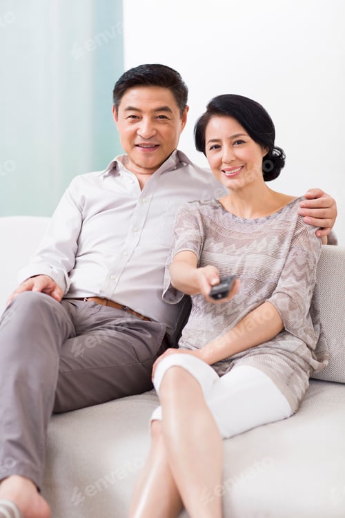 Preview: Cheerful mature couple watching TV at home