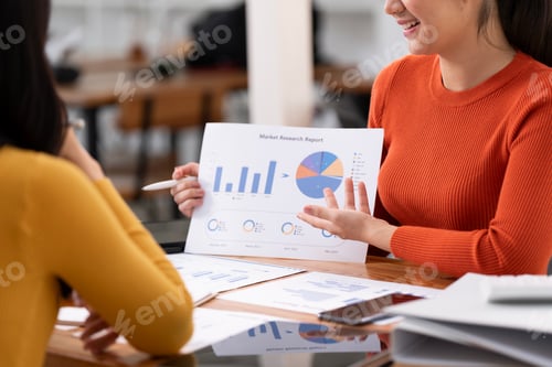 Preview: Two business women sit at desk discuss project details