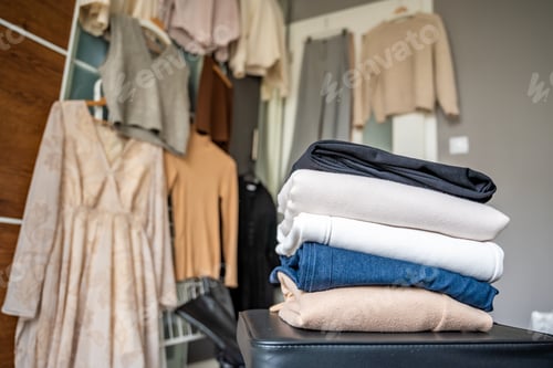 Preview: Stacked pile of clothing prepared for resale, donation, or recycling, with wardrobe with outfits in