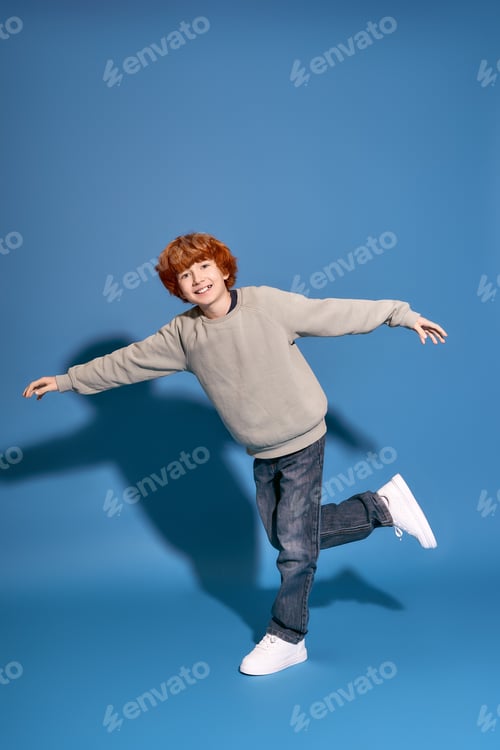 Preview: Playful and stylish young boy dances joyfully against a bright blue background