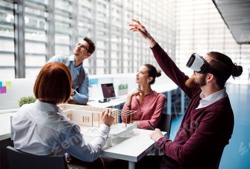 Preview: Group of young architects with model of a house and VR goggles working in office.