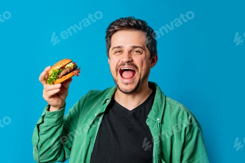 Preview: Smiling white guy in green shirt with hamburger on blue background