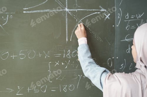 Preview: Hand of young female student in hijab pointing at drawn graph while solving equation by blackboard