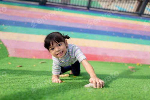 Preview: Cute Asian girl having fun trying to climb on artificial boulders at schoolyard playground,