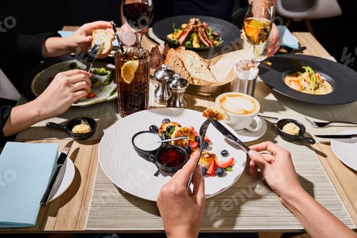 Preview: cropped view of woman eating delicious syrniki during dinner with friends in restaurant