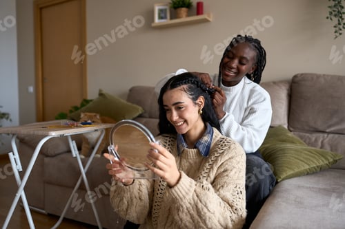 Preview: Young woman getting her hair braided by her friend at home