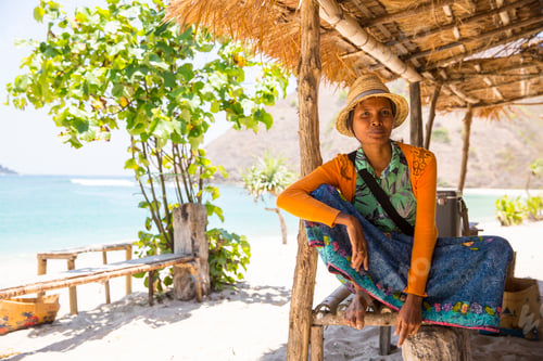 Preview: A person relaxes under a thatched shade with a serene beach backdrop