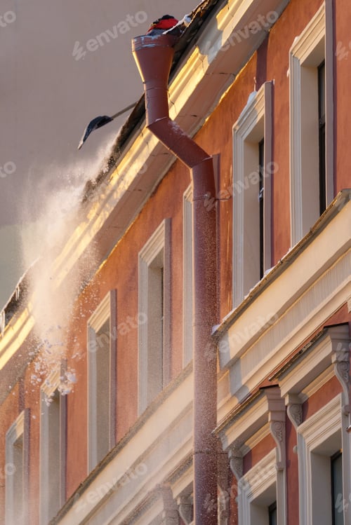 Preview: Ice dam prevention. Man holding shovel cleaning roof from snow, ice and icicles during wintertime