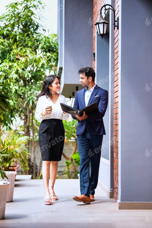 Preview: Indian coworkers in formal attire talk and walk outside modern office holding file and coffee